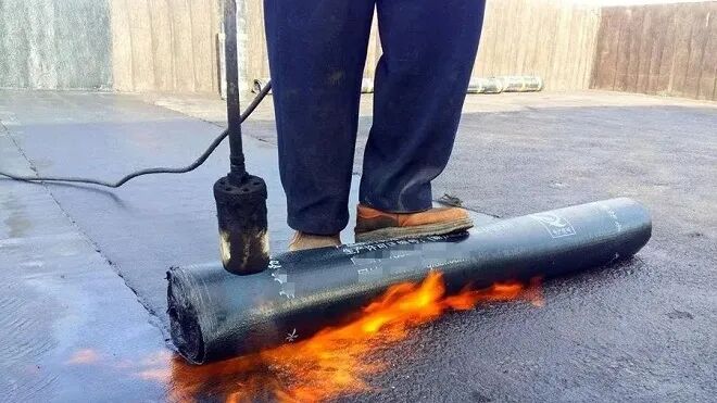 Torch flame heating the underside of an SBS waterproofing membrane roll