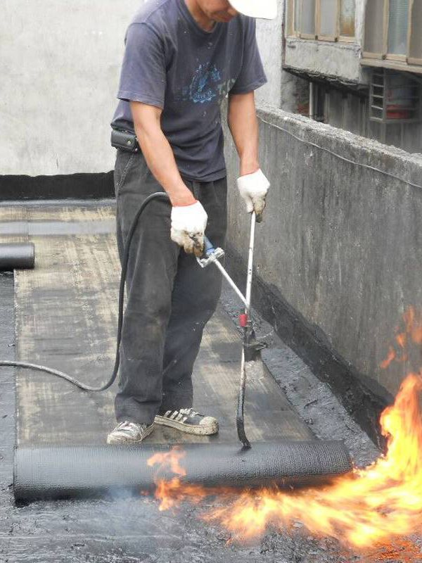 Worker torching SBS waterproofing membrane up to the wall-parapet edge